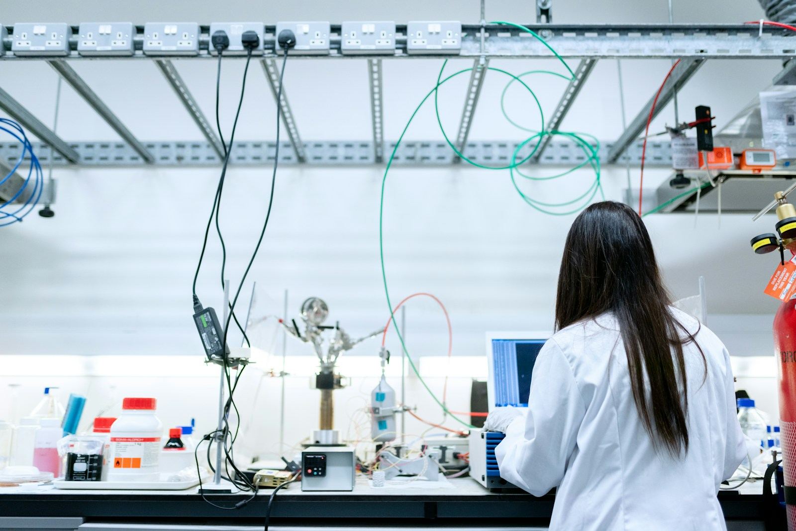 Wissenschaftlerin im Laborkittel an einem Laborarbeitsplatz mit Laptop – in Laborgebäuden trennen Druckstufen Labore, Flure und Schleusen
